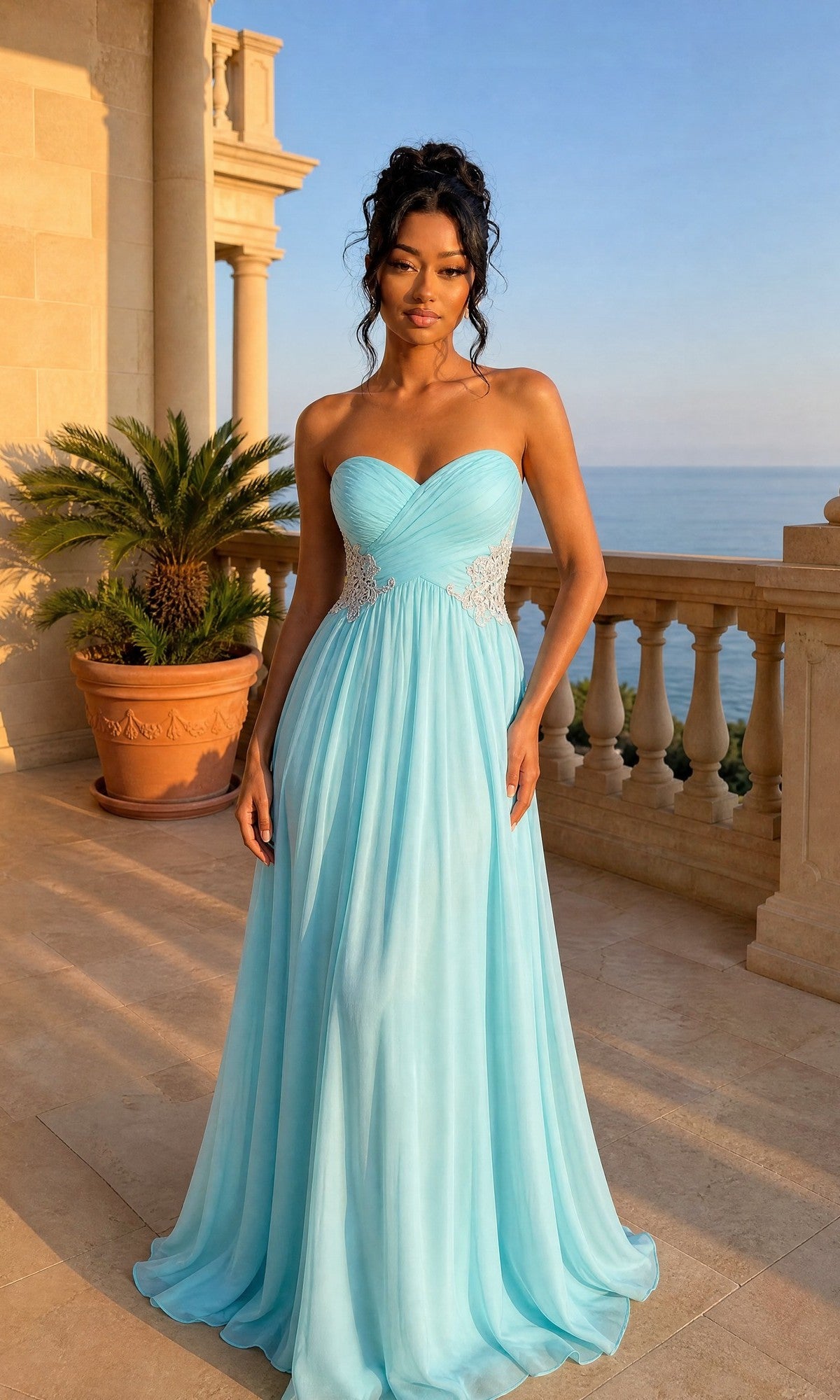 A woman wears the La Femme Dress 21331 in Caribbean Green, a long chiffon strapless gown with embroidered sides, standing on a sunlit stone terrace with a potted palm, balustrade, and sea view in the background.